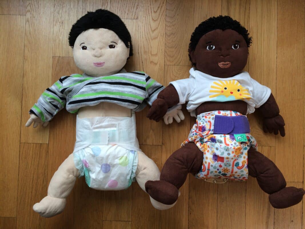 Das Foto zeigt links eine Puppe in einer Einwegwindel. Die Puppe rechts trägt eine Totsbots-Stoffwindel.